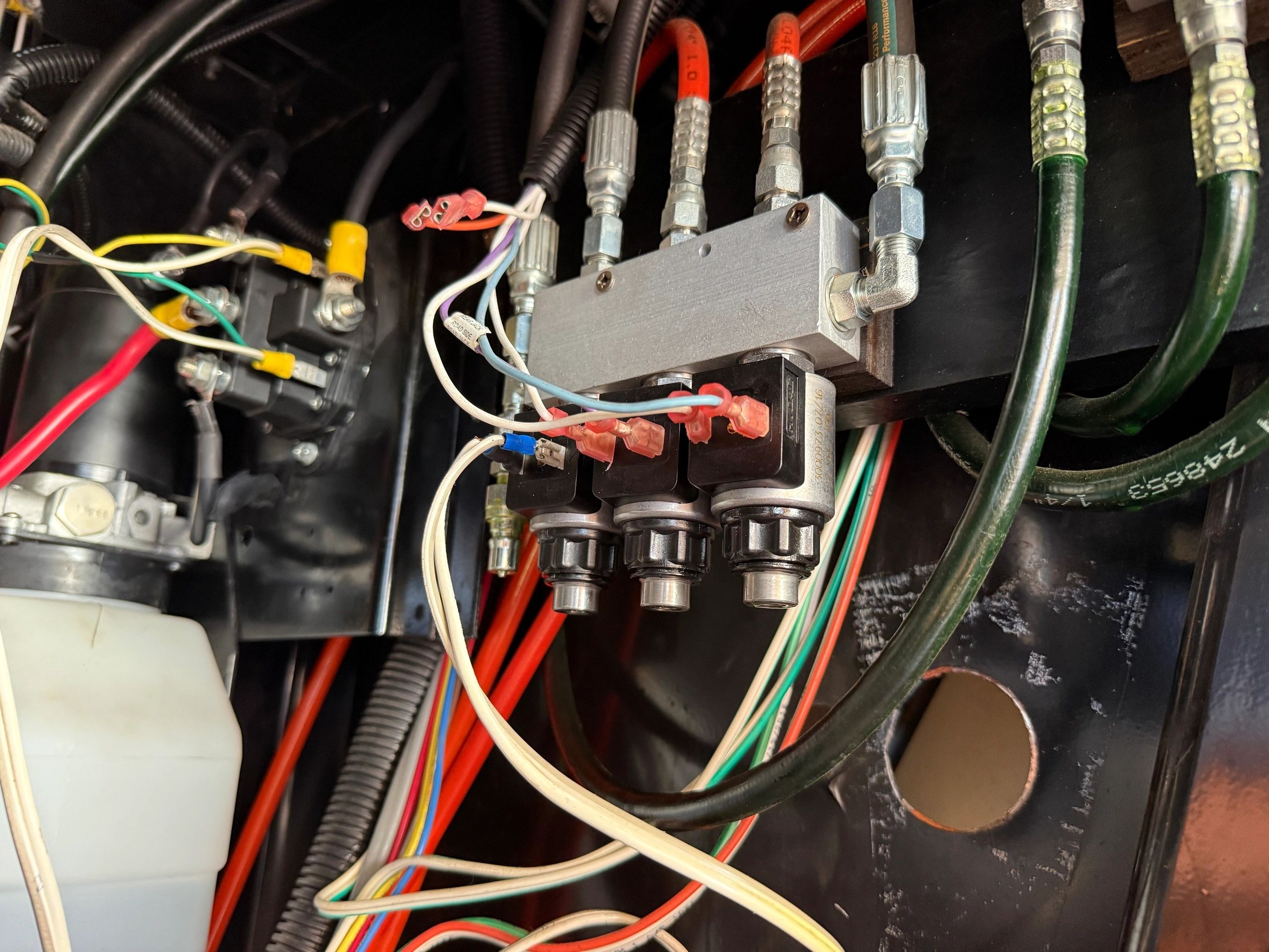 Close view of an RV hydraulic manifold with three solenoid valves, braided pressure hoses and coloured wiring.